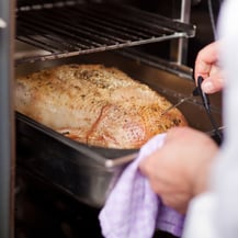 Closeup of chefs hands checking temperature of grilled turkey in commercial kitchen