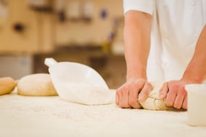 Baker kneading dough at a counter in a commercial kitchen